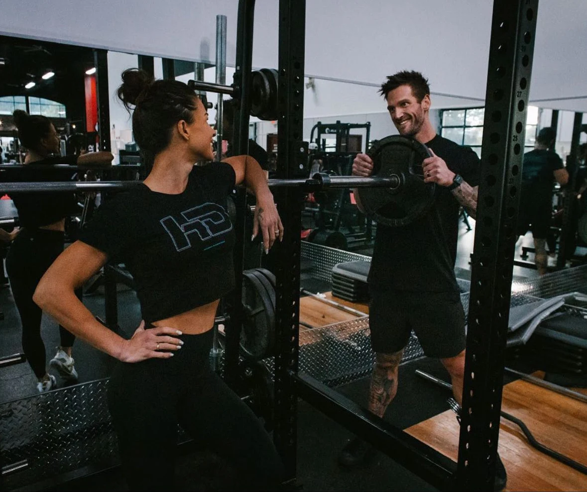 A Trademark coach and athlete talk beside a squat rack